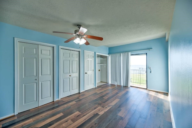 unfurnished bedroom featuring a textured ceiling, dark wood-style flooring, a ceiling fan, multiple closets, and access to outside