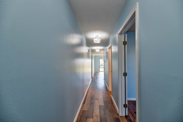 hallway featuring a textured wall, wood finished floors, and baseboards