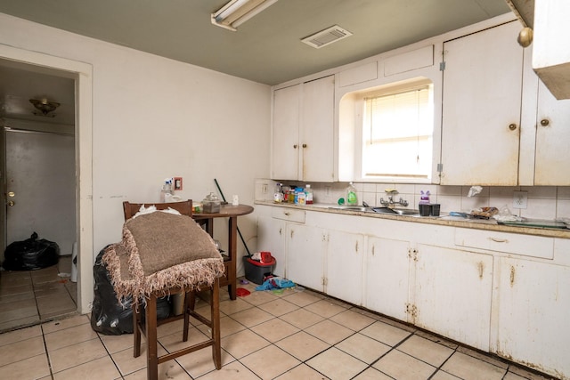 kitchen featuring light tile patterned floors, a sink, visible vents, white cabinetry, and tasteful backsplash