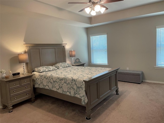 bedroom featuring a raised ceiling, light colored carpet, ceiling fan, and baseboards