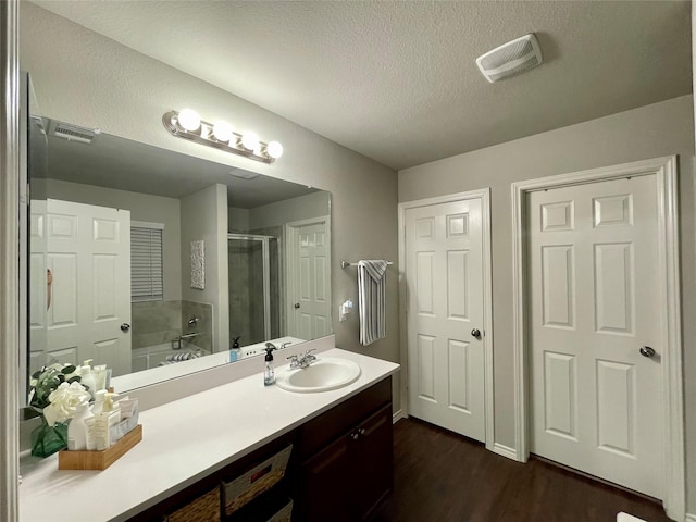 full bath with wood finished floors, visible vents, a textured ceiling, a shower stall, and vanity