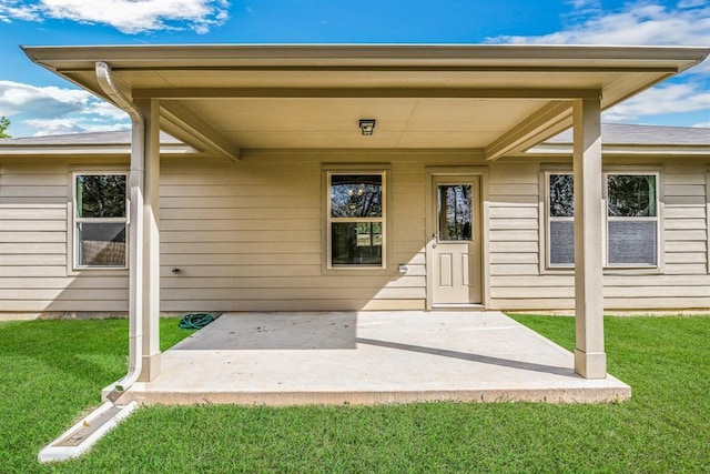 view of exterior entry with a lawn and a patio area