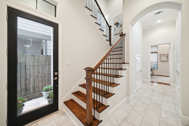 staircase with arched walkways, a high ceiling, visible vents, and baseboards