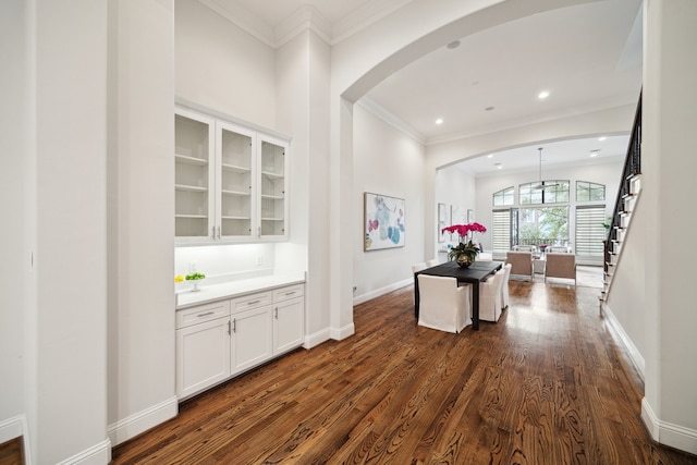 corridor with dark wood-style floors, baseboards, arched walkways, and ornamental molding