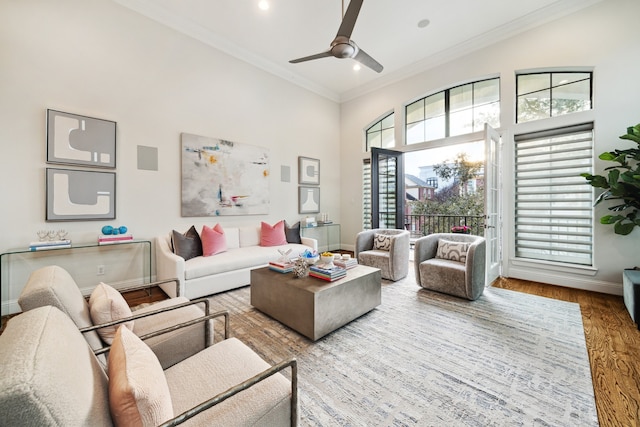 living room featuring a towering ceiling, ornamental molding, a ceiling fan, wood finished floors, and baseboards