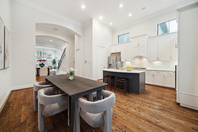 dining room with arched walkways, baseboards, ornamental molding, stairway, and light wood-type flooring