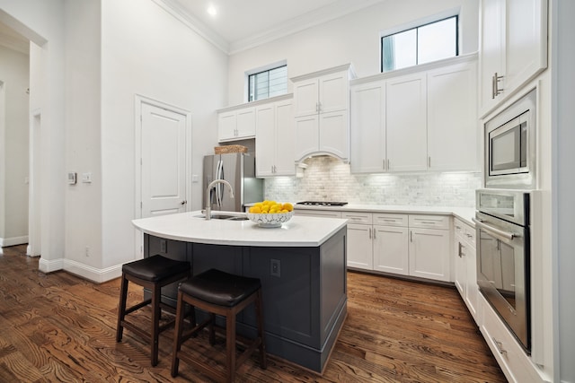 kitchen with tasteful backsplash, a center island with sink, stainless steel appliances, crown molding, and a kitchen bar