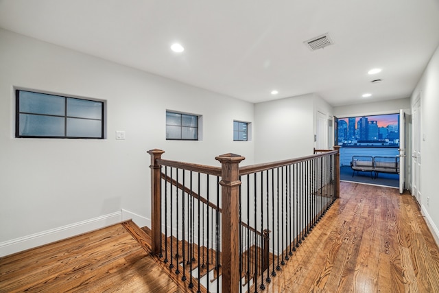 hallway featuring baseboards, visible vents, an upstairs landing, and wood finished floors