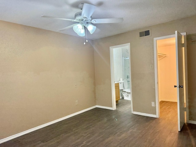 unfurnished bedroom with baseboards, visible vents, dark wood-type flooring, a walk in closet, and a closet