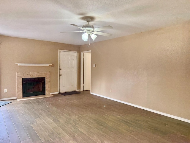 unfurnished living room with ceiling fan, a textured ceiling, a premium fireplace, wood finished floors, and baseboards