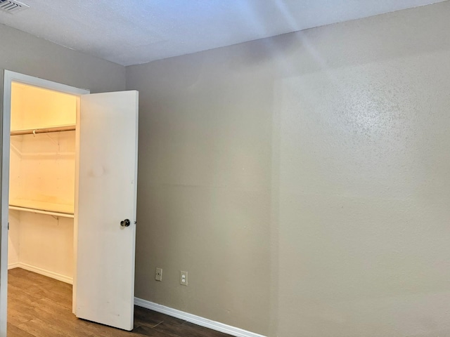 unfurnished bedroom with a walk in closet, a closet, visible vents, and wood finished floors