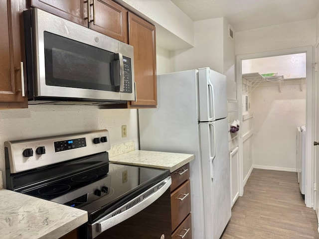 kitchen featuring stainless steel appliances, visible vents, baseboards, light wood-style floors, and brown cabinets