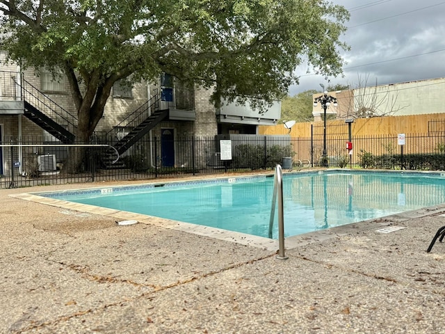 community pool featuring stairs, central AC unit, and fence