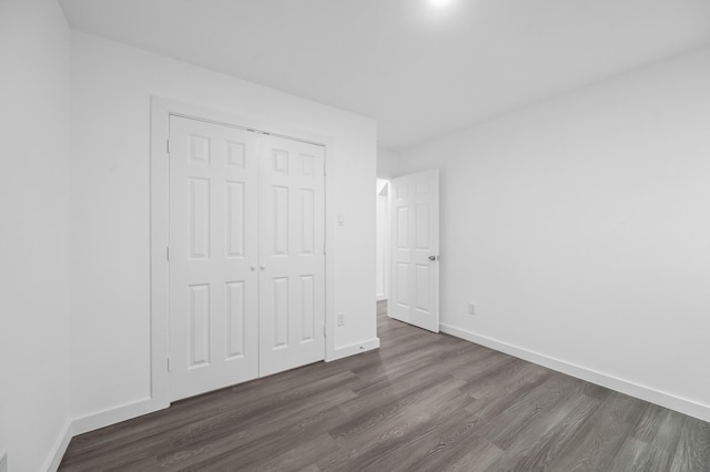 unfurnished bedroom with dark wood-type flooring, a closet, and baseboards