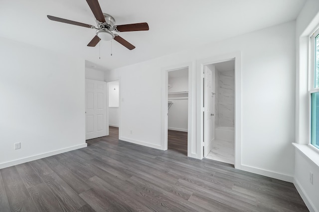 unfurnished bedroom with a closet, a spacious closet, connected bathroom, wood finished floors, and baseboards