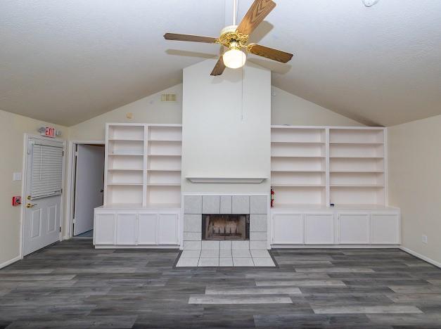 unfurnished living room with a ceiling fan, a tile fireplace, dark wood-style flooring, and lofted ceiling