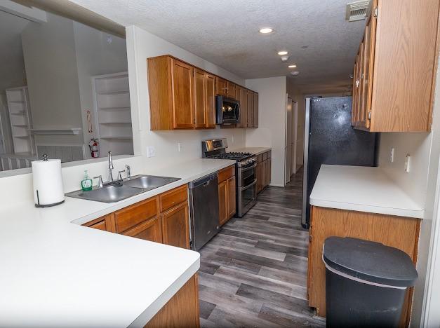 kitchen featuring dishwashing machine, a peninsula, a sink, double oven range, and brown cabinetry