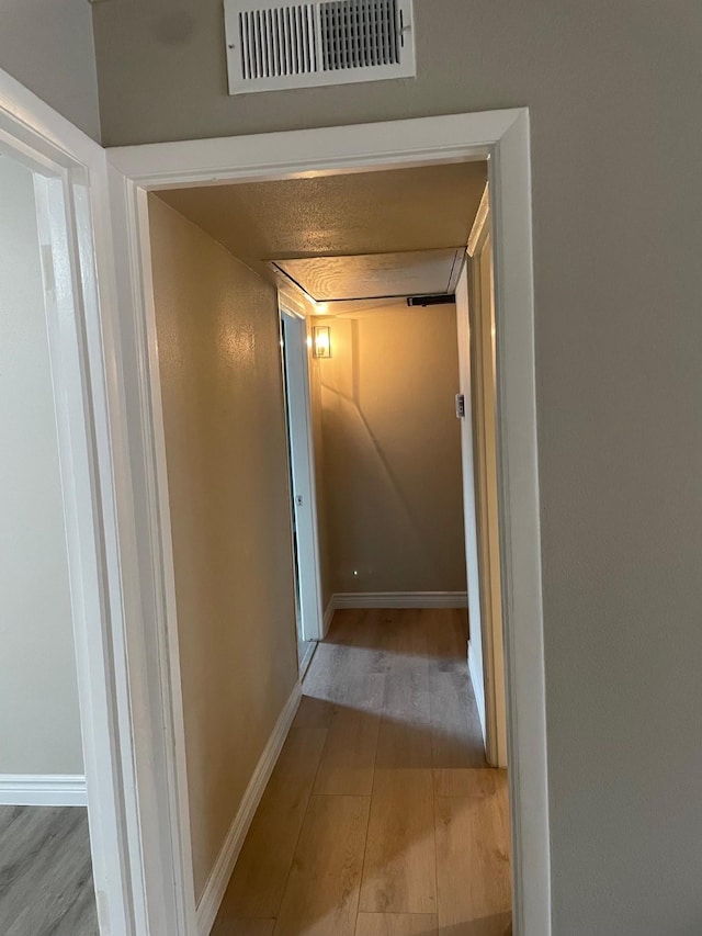 hall featuring visible vents, baseboards, and wood finished floors