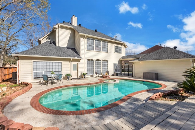 rear view of property featuring a patio, an in ground hot tub, fence, roof with shingles, and a chimney