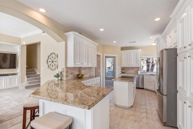 kitchen featuring a peninsula, white cabinets, stainless steel appliances, and light stone counters