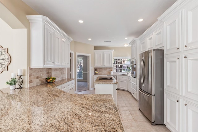 kitchen featuring light tile patterned floors, appliances with stainless steel finishes, light stone countertops, white cabinetry, and backsplash