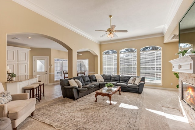 living area with arched walkways, baseboards, a tile fireplace, ceiling fan, and ornamental molding