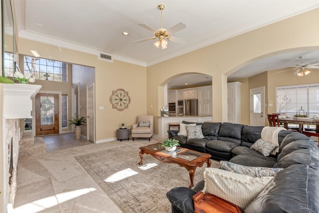 living room with baseboards, visible vents, arched walkways, a ceiling fan, and ornamental molding