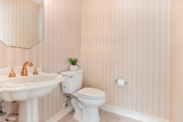 half bathroom with baseboards, wallpapered walls, toilet, and tile patterned floors