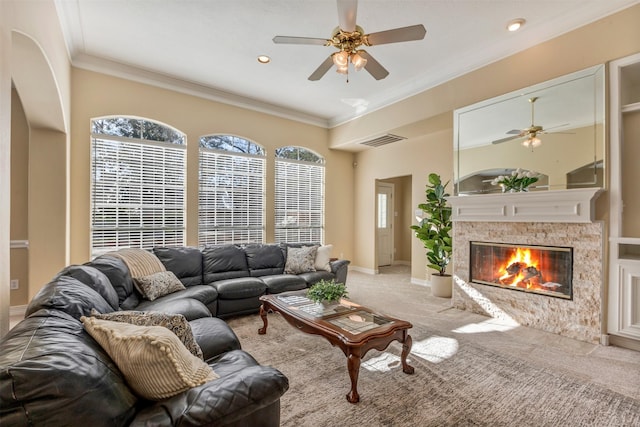 carpeted living area with ceiling fan, visible vents, baseboards, a glass covered fireplace, and crown molding