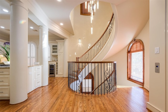 staircase with wood finished floors, plenty of natural light, beverage cooler, and ornamental molding