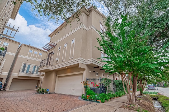 view of property featuring a balcony, stucco siding, decorative driveway, and a garage