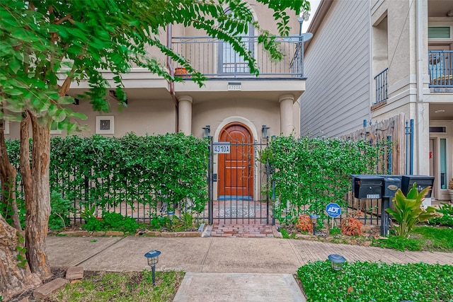 doorway to property featuring stucco siding, a balcony, and fence