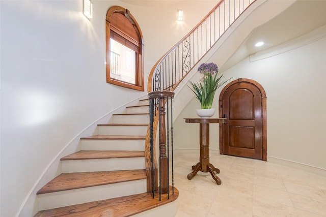 stairs featuring arched walkways, baseboards, and a towering ceiling