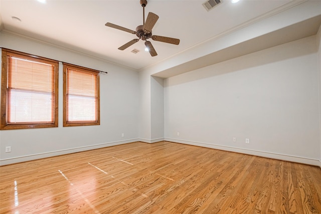 empty room with light wood-type flooring, visible vents, baseboards, and crown molding