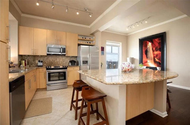 kitchen with stainless steel appliances, light brown cabinets, ornamental molding, and a kitchen breakfast bar