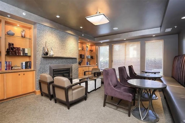 interior space with built in features, a tray ceiling, light colored carpet, and a fireplace