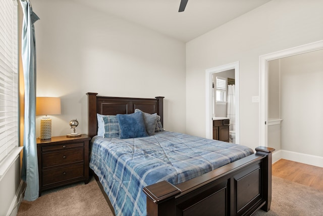 bedroom with a ceiling fan, ensuite bath, light colored carpet, and baseboards