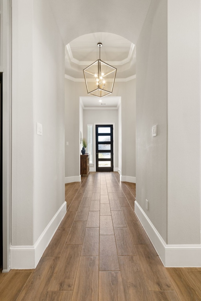 foyer entrance featuring arched walkways, a raised ceiling, wood finished floors, and a chandelier