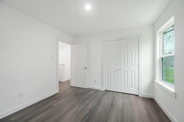 unfurnished bedroom featuring dark wood-style floors, a closet, multiple windows, and baseboards