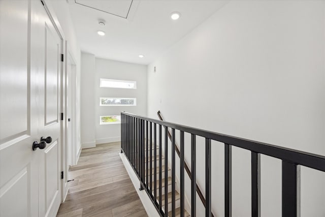 hall featuring light wood-style floors, recessed lighting, baseboards, and an upstairs landing