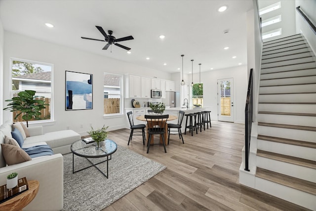 living room featuring light wood finished floors, baseboards, ceiling fan, stairway, and recessed lighting