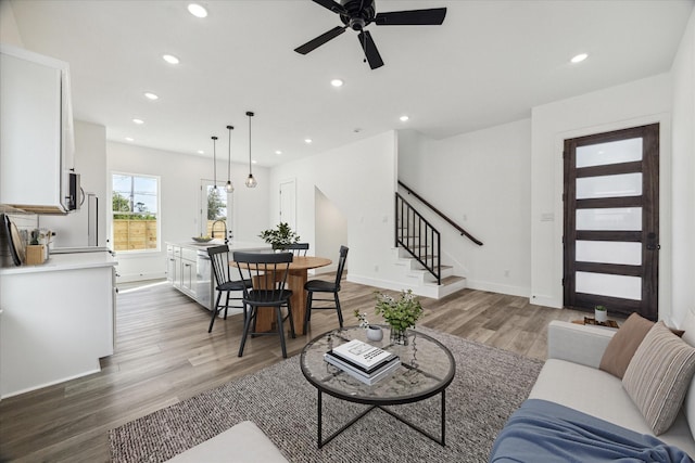 living room featuring stairs, baseboards, wood finished floors, and recessed lighting