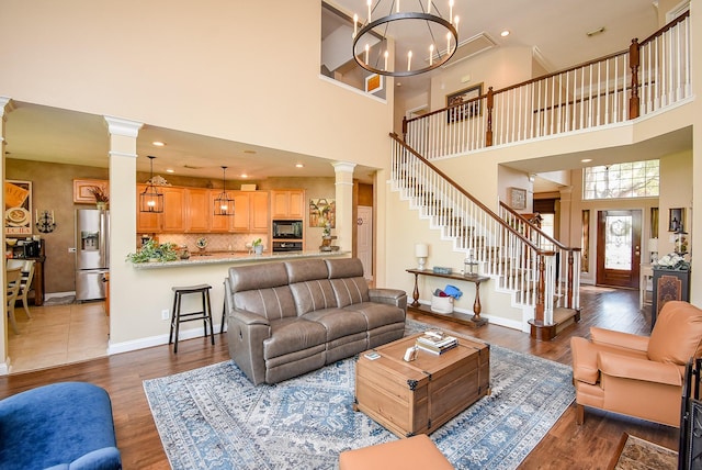 living area featuring dark wood-style flooring, baseboards, a chandelier, stairs, and ornate columns