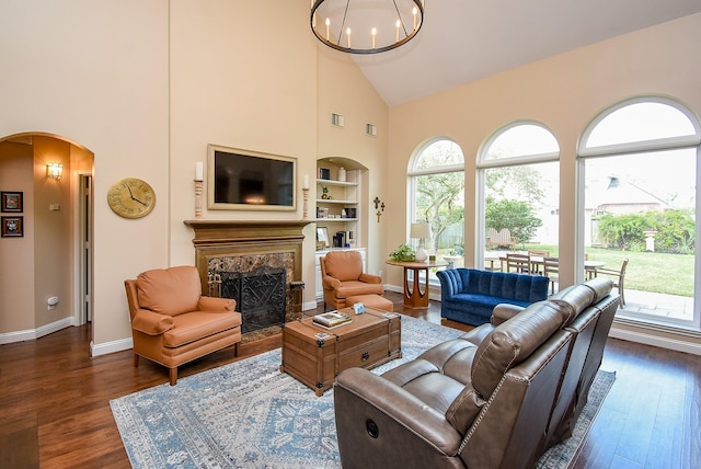 living area featuring baseboards, a chandelier, a fireplace, arched walkways, and dark wood-style flooring