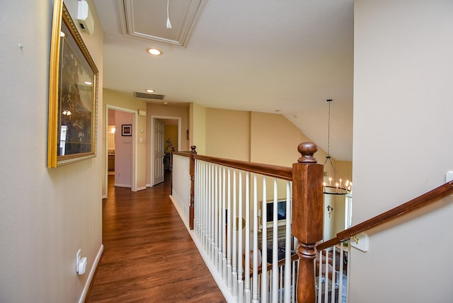 hallway with visible vents, wood finished floors, an inviting chandelier, baseboards, and attic access