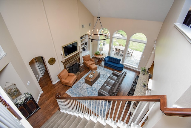 living area with a notable chandelier, high vaulted ceiling, wood finished floors, arched walkways, and a fireplace