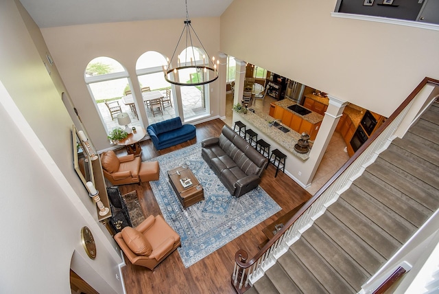 living room featuring a notable chandelier, high vaulted ceiling, wood finished floors, and ornate columns