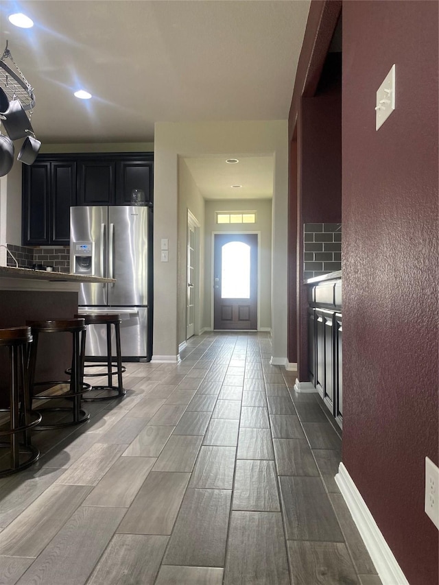 kitchen featuring dark cabinetry, baseboards, stainless steel refrigerator with ice dispenser, and backsplash