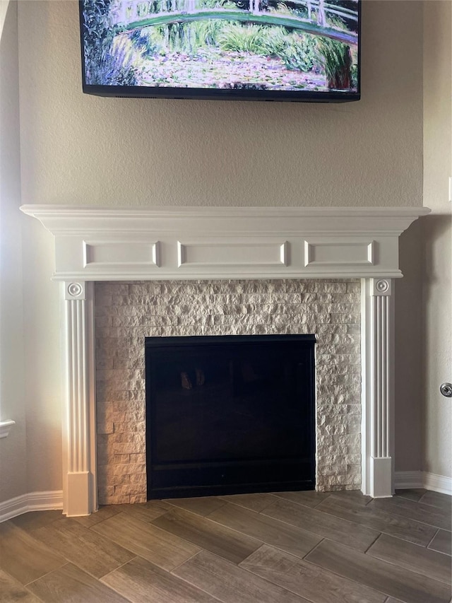 interior details featuring a tiled fireplace, baseboards, and wood finish floors