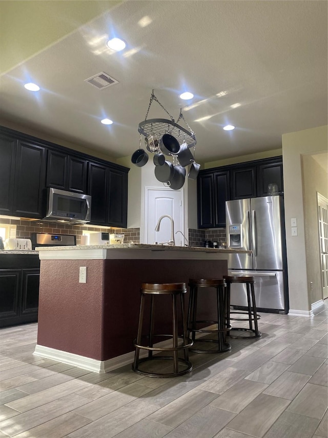 kitchen featuring visible vents, a breakfast bar, dark cabinets, appliances with stainless steel finishes, and tasteful backsplash